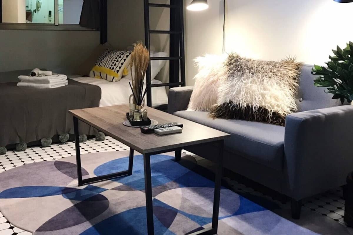 A cozy room with a bunk bed, a sofa, a coffee table, and a floor lamp. There are framed pictures on the wall and a potted plant on the sofa.