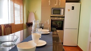 Een moderne keuken met een eettafel voor vier personen, een magnetron, oven en een koelkast.