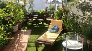 Een terras met een lounge stoel, een kleine tafel en potplanten.