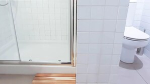Un baño con cabina de ducha de vidrio, inodoro blanco y paredes cubiertas de azulejos blancos.