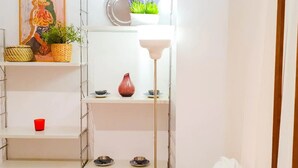 Una habitación con paredes blancas, un cuadro, estantes con objetos decorativos y una lámpara de pie.