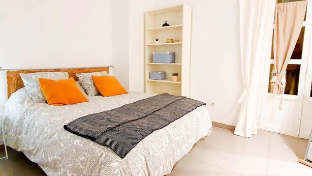 Un dormitorio con cama, una mesita de noche y una ventana con cortinas.