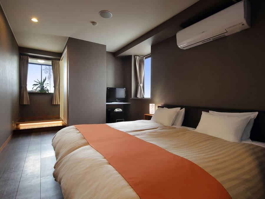 A hotel room with a large bed, a flat-screen TV, a desk, and a window with curtains.