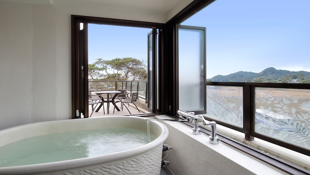A bathroom with a large bathtub, a window with a view of a balcony and mountains. - Yumemisaki (Minamiboso)