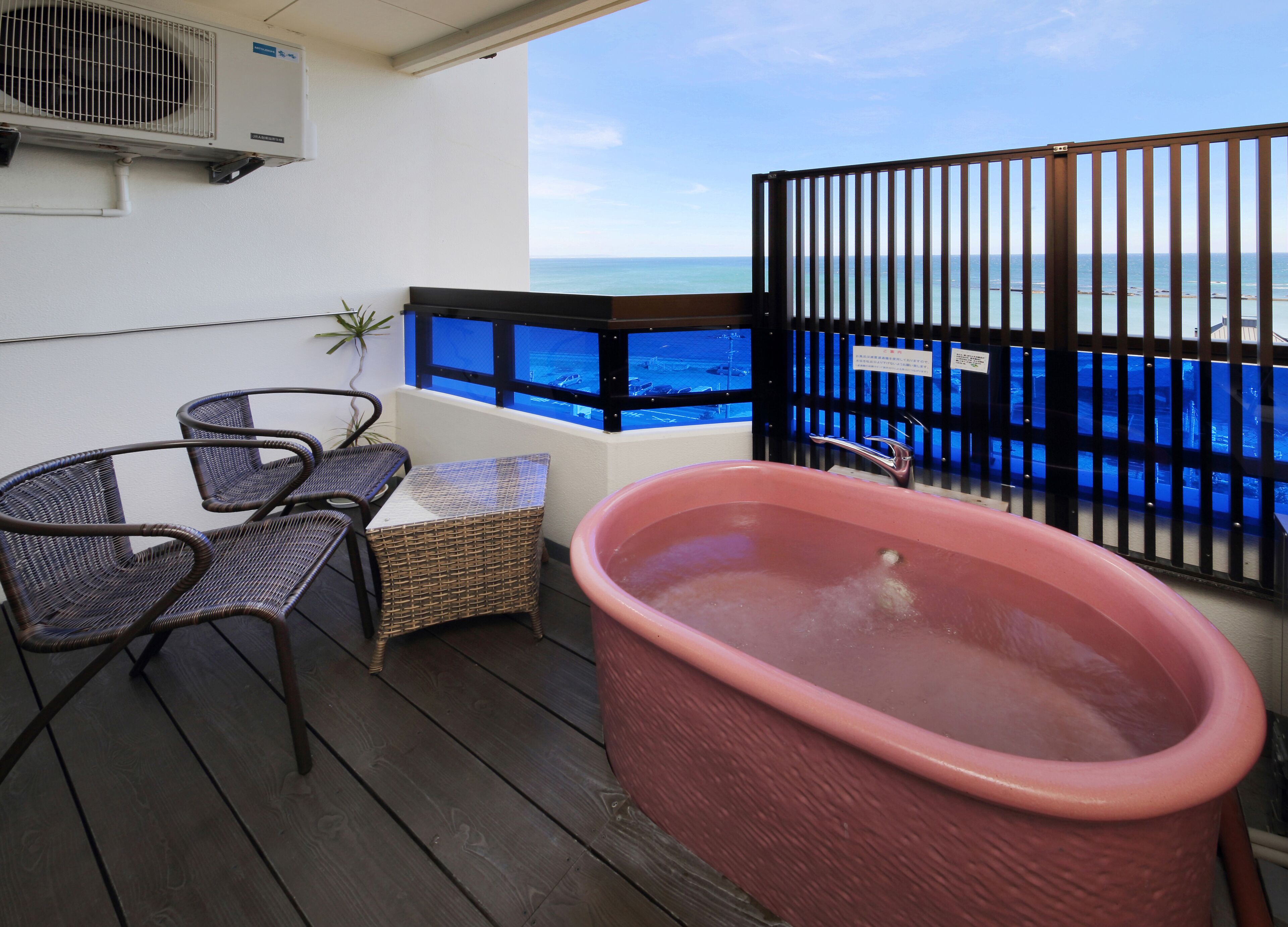 A balcony with a wicker table and chairs, a large bathtub, and a view of the ocean.