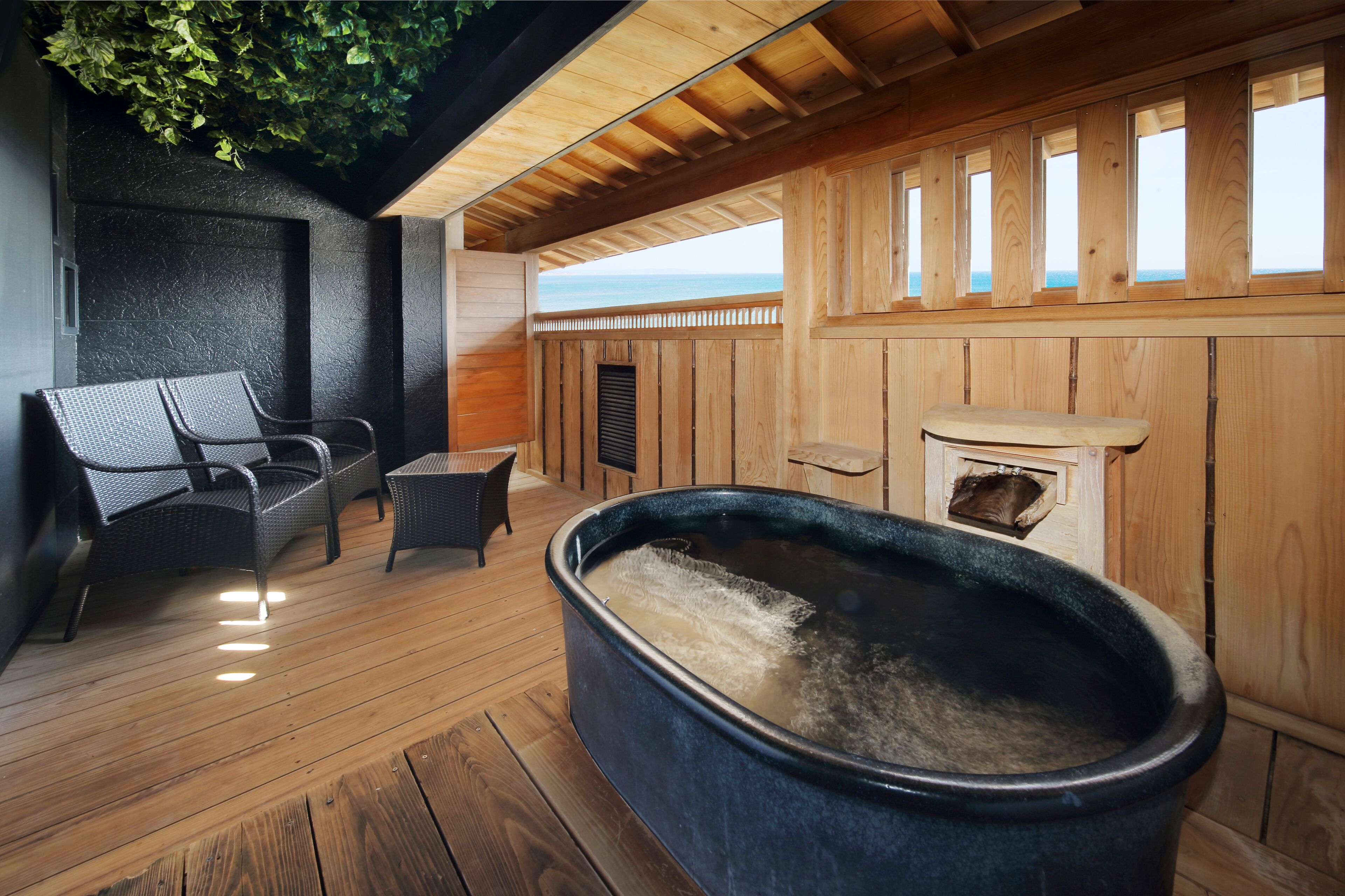 Una terraza de madera con un jacuzzi, sillas de mimbre y vista al océano.