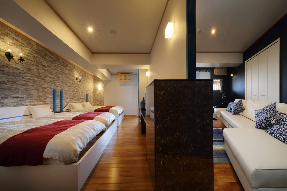A modern hotel room with a large bed, a sofa, and a marble accent wall.