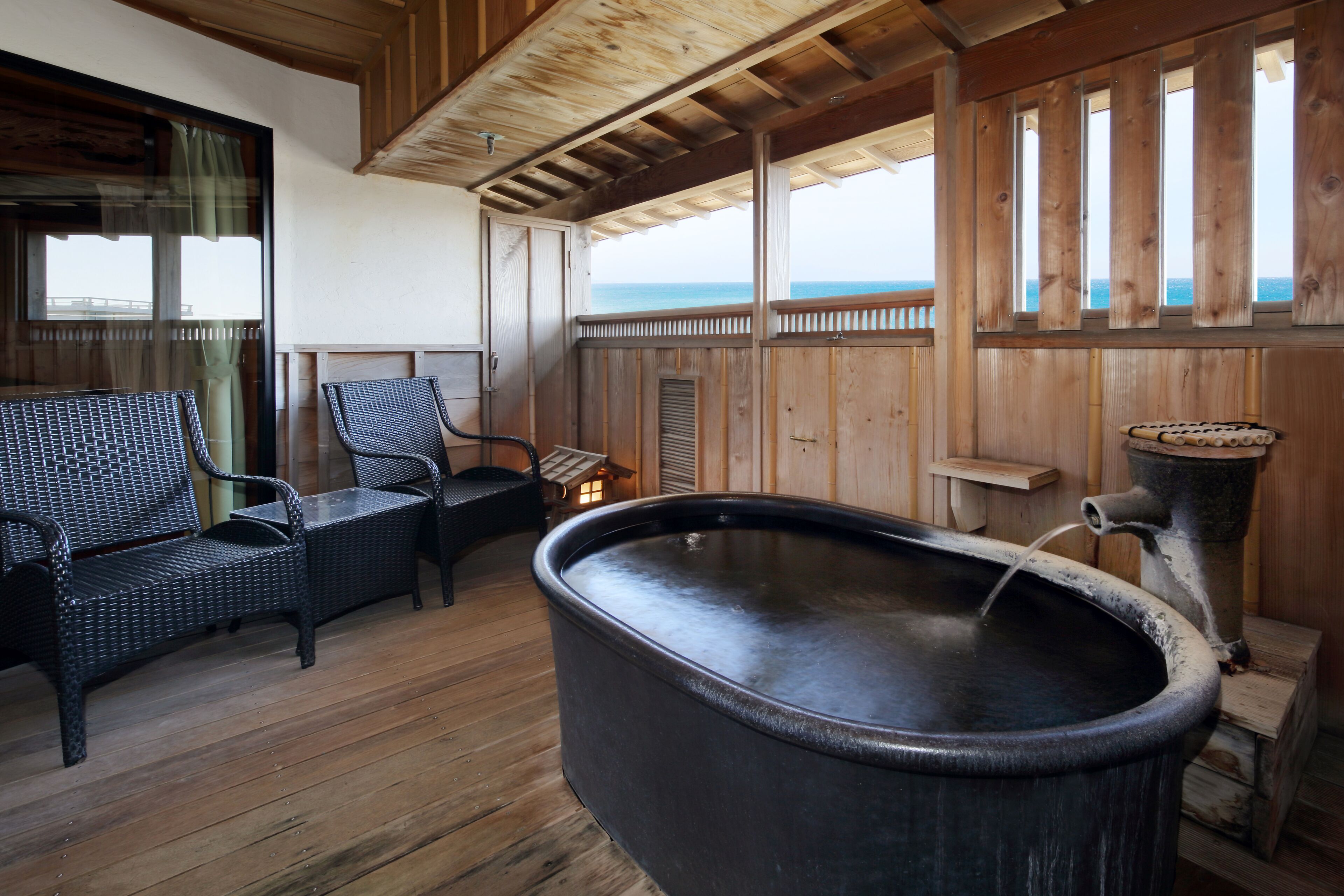 A wooden deck with a hot tub, wicker furniture, and a view of the sea.