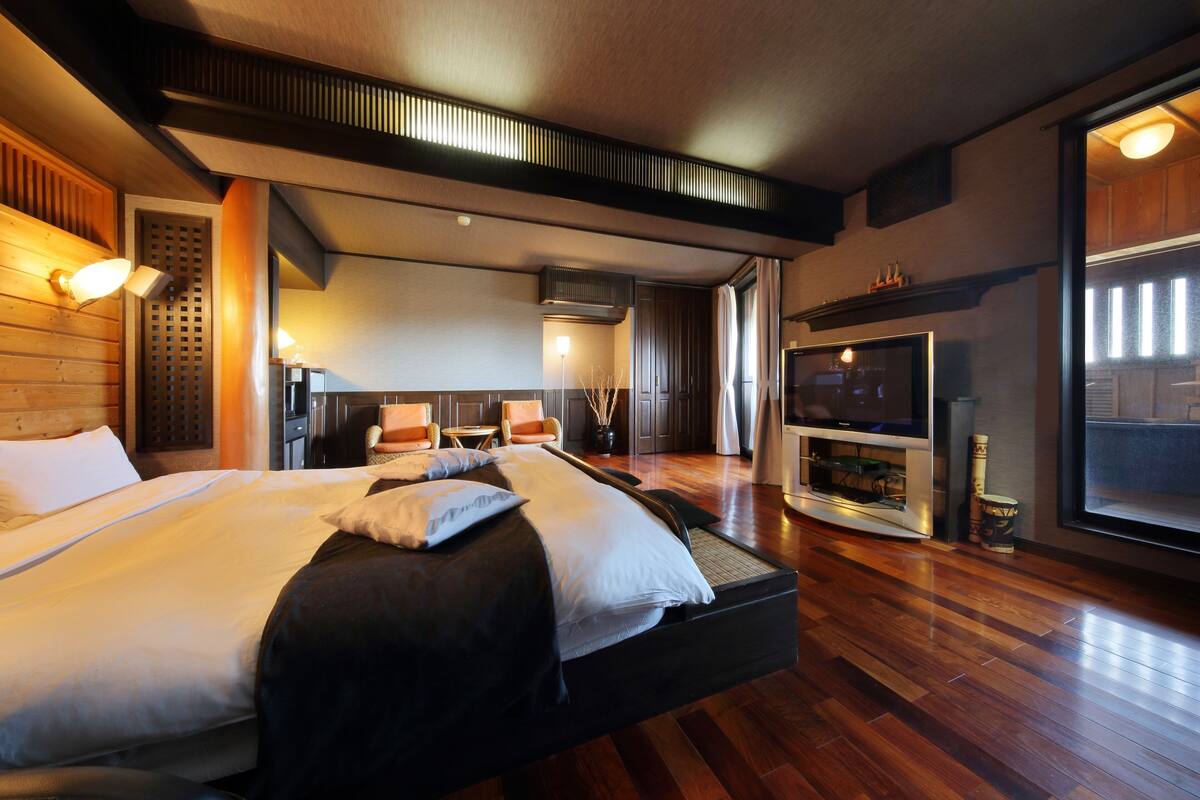 A hotel room with a large bed, a TV, and a wooden floor.