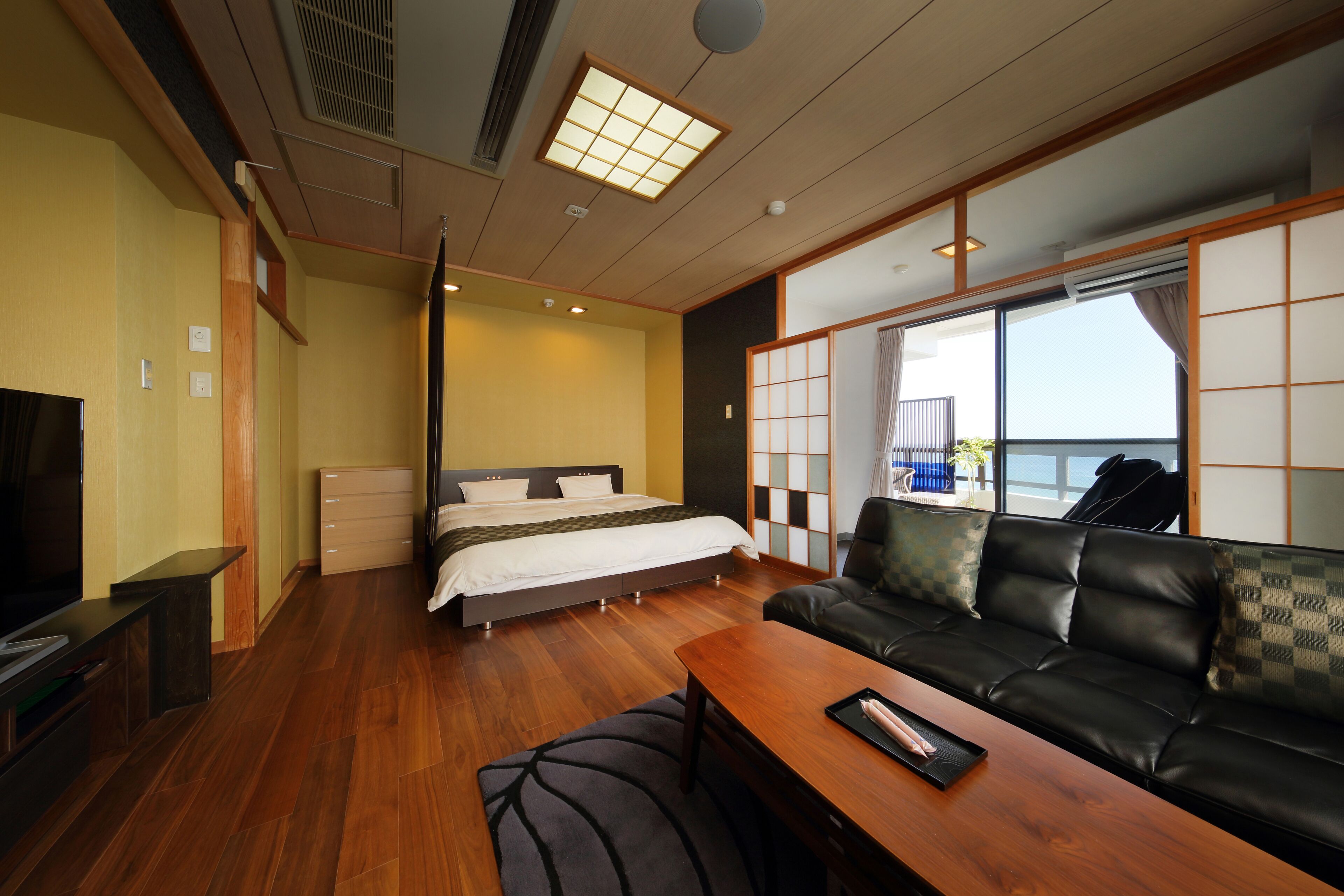 A hotel room with a bed, a sofa, a TV, and a wooden table.
