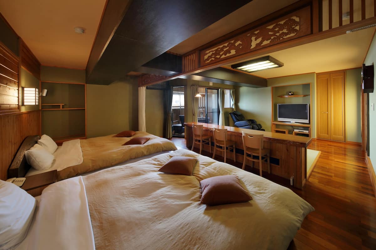 A hotel room with two beds, a desk with a chair, a television, and a wooden ceiling.