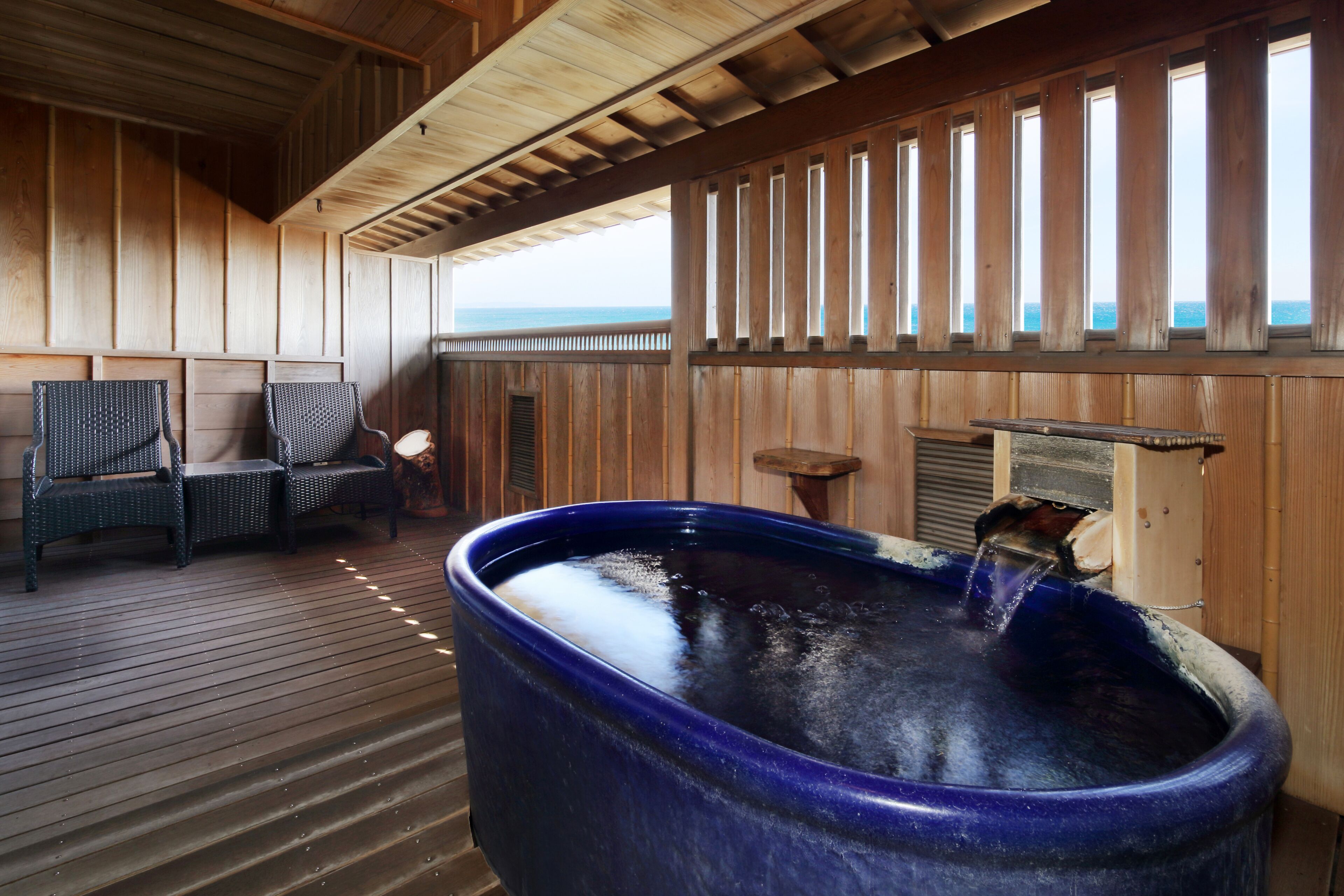 Un terrazzo in legno con una vasca idromassaggio, una zona salotto e vista sull'oceano.
