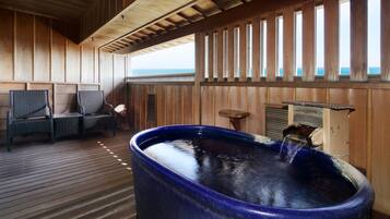 Un terrazzo in legno con una vasca idromassaggio, una zona salotto e vista sull'oceano.