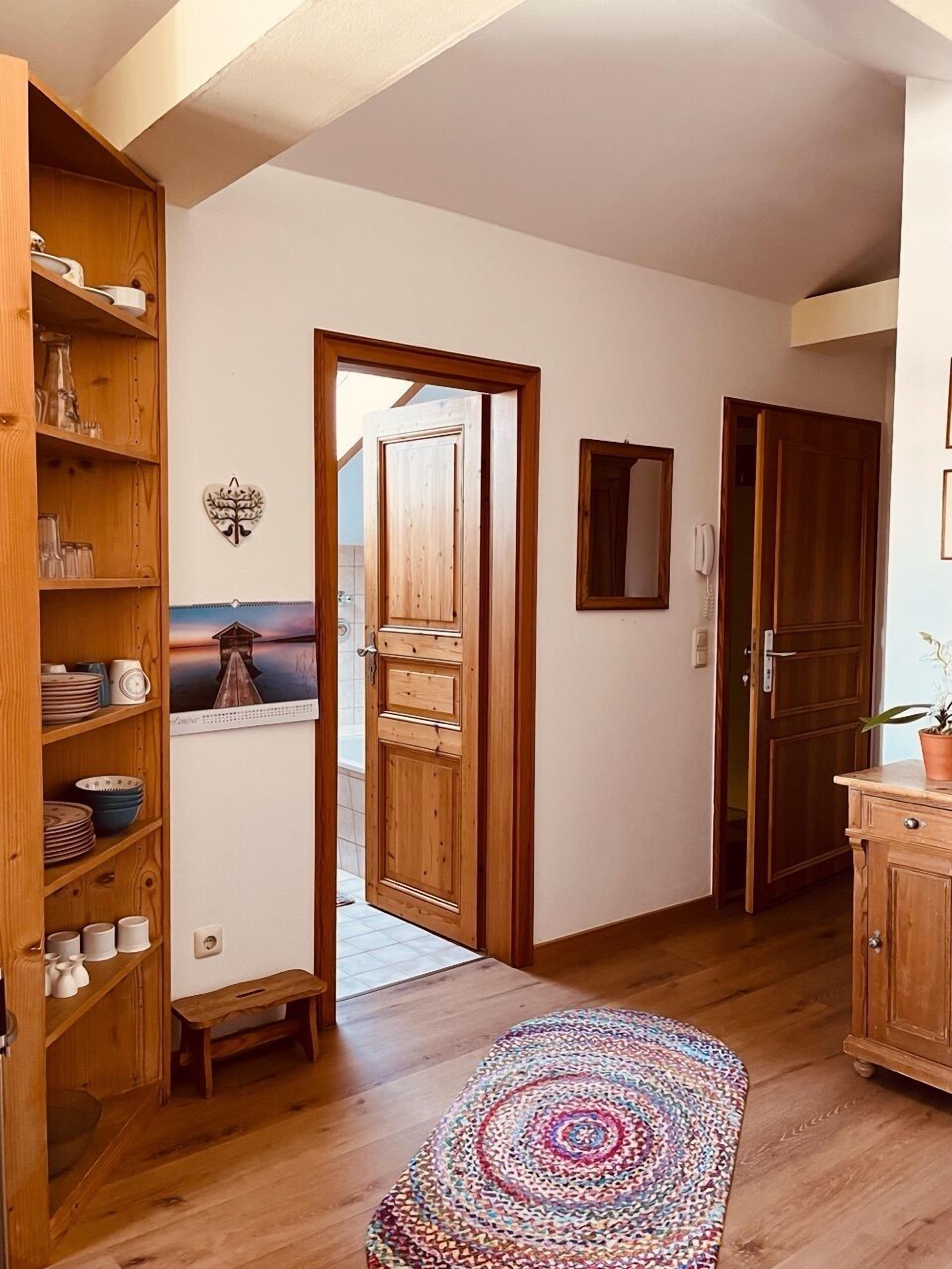 A hallway with wooden shelving, a door, a small bench, and a colorful rug.