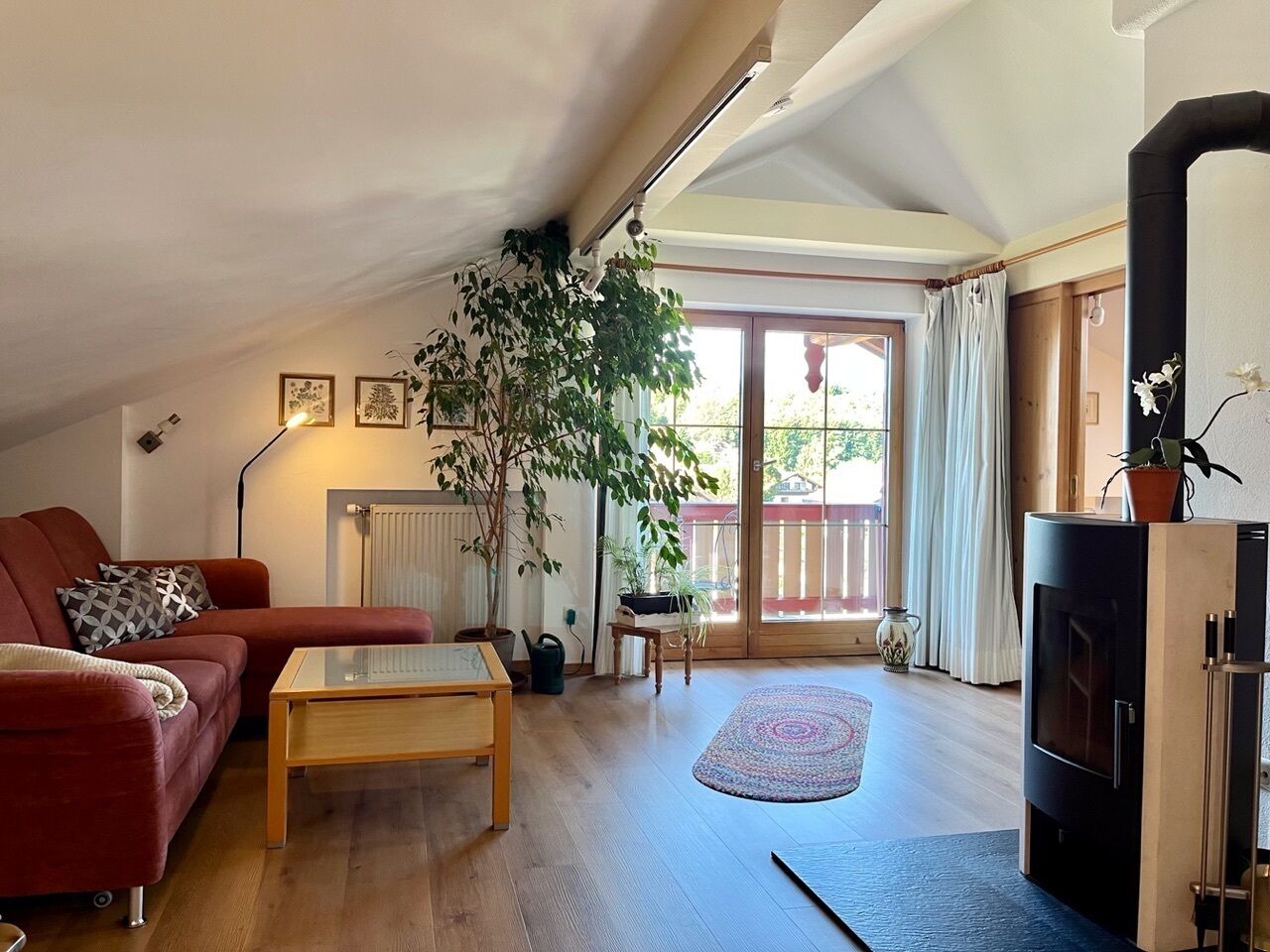 A cozy living room with a red sofa, a wooden coffee table, a fireplace, and a large window with curtains.