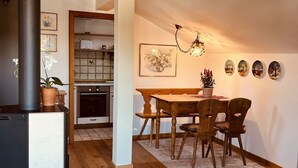 A modern kitchen with a dining area, featuring a wooden table and chairs, a black stove, and a hanging light fixture. - Ferienwohnung, Nr. 2, 48 qm Dachgeschoss, 1 Separates Schlafzimmer (Bad Endorf)