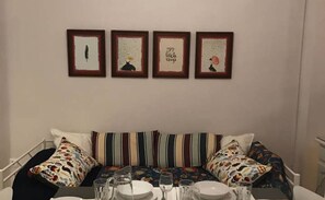 A dining area with a table set for four, a striped sofa, and four framed artworks on the wall.