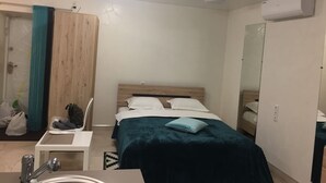 Et soveværelse med sengegavl i træ, seng med hvide sengetøj, et lille bord med stol, et spejl og en aircondition på væggen.