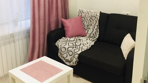 En hyggelig stue med god belysning, et hvidt sofabord, en sort sofa med mønstrede puder og en lyserød gardin.