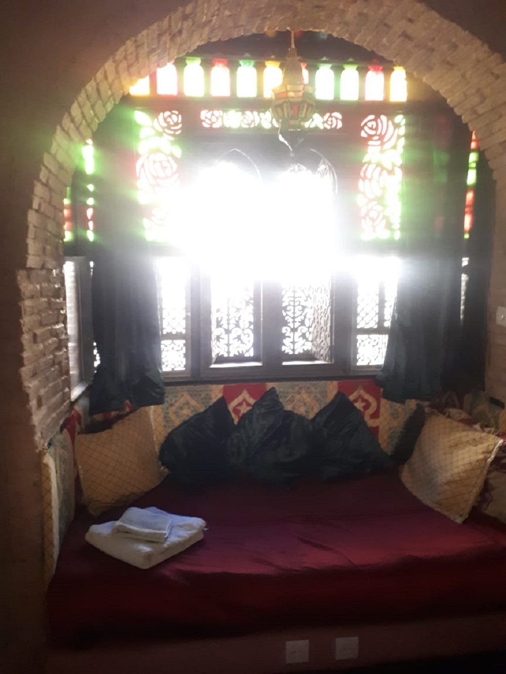 Ein Zimmer mit einer Ziegelbogenkonstruktion, einem Fenster mit farbigem Glas und einem roten Sofa mit Kissen.