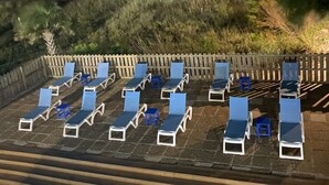 Zona de piscina con sillones de descanso y vista al océano bajo un cielo nublado.