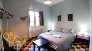 Una camera da letto con un letto, una sedia, un tavolo, una finestra con tende e due lampade a parete.