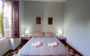 Hotelkamer met een groot bed, twee nachtkastjes, twee lampen, twee ingelijste foto’s aan de muur en een raam met gordijnen.