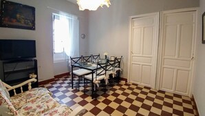 Una stanza con pavimento a scacchi, un tavolo da pranzo con sedie, una televisione, un divano e una porta.