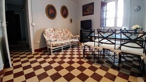 Zona pranzo con pavimento a scacchi, un divano floreale e un tavolo con sedie.