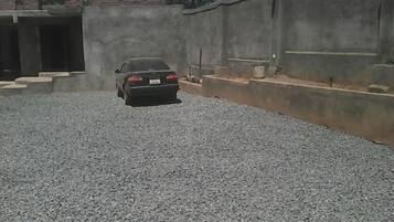 Un coche aparcado en un área de grava con un muro de hormigón y escaleras que suben a la entrada de un edificio.