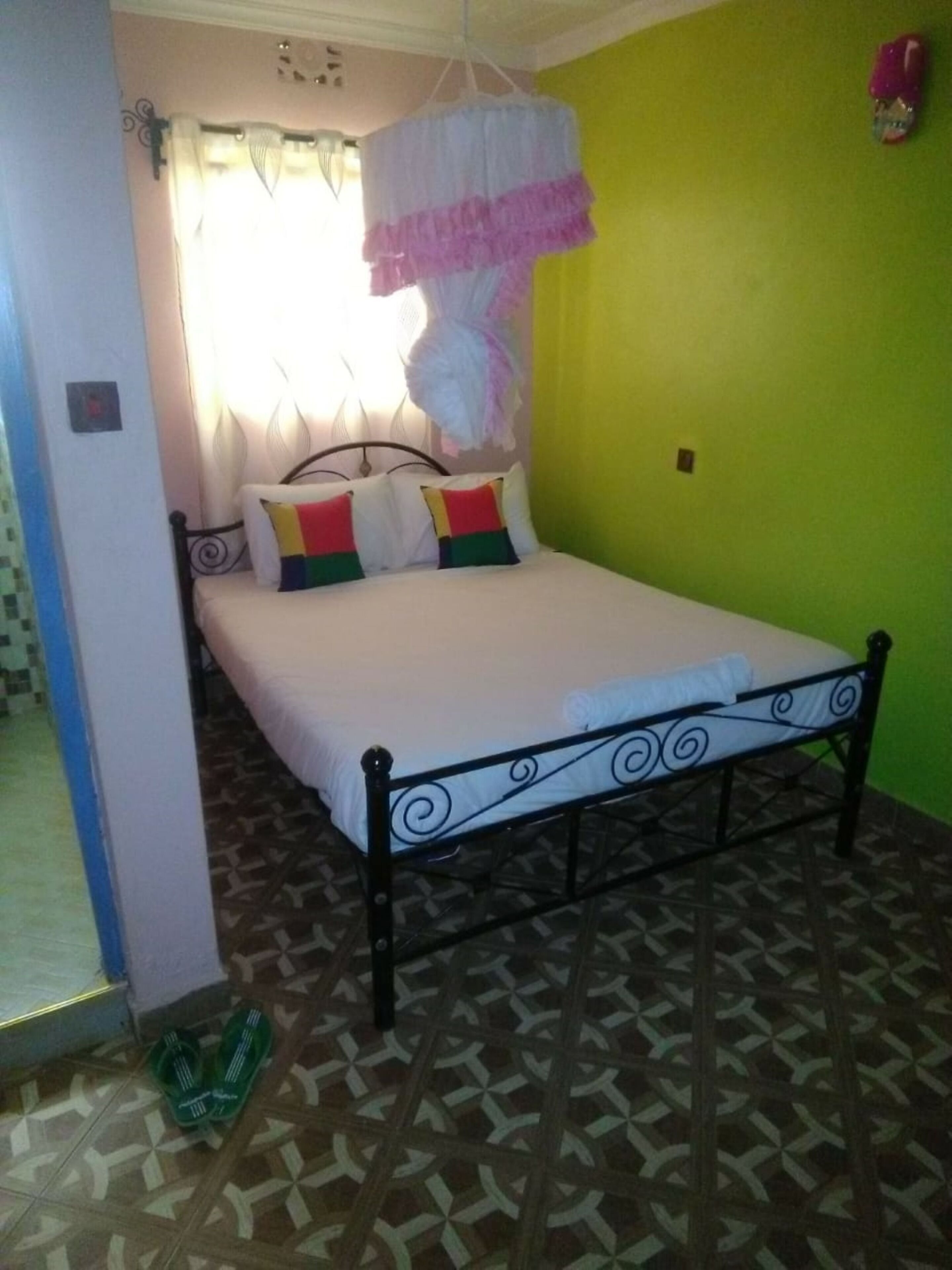 Una cama con colchón blanco, almohadas coloridas, estructura metálica y mosquitera colgante.