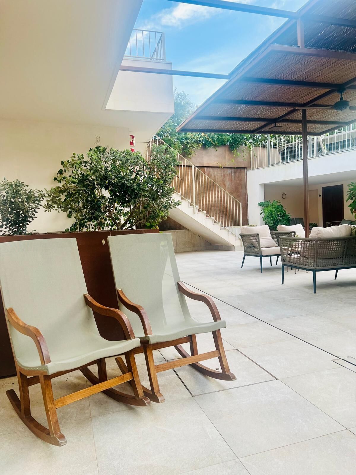 A covered outdoor seating area with a glass ceiling, a staircase, and potted plants.