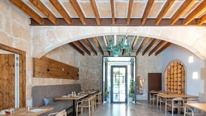 An interior with stone walls, wooden beams, and a central archway leading to a door. Tables and chairs are arranged for dining. - Ynaira Hotel & Spa (Ariany)