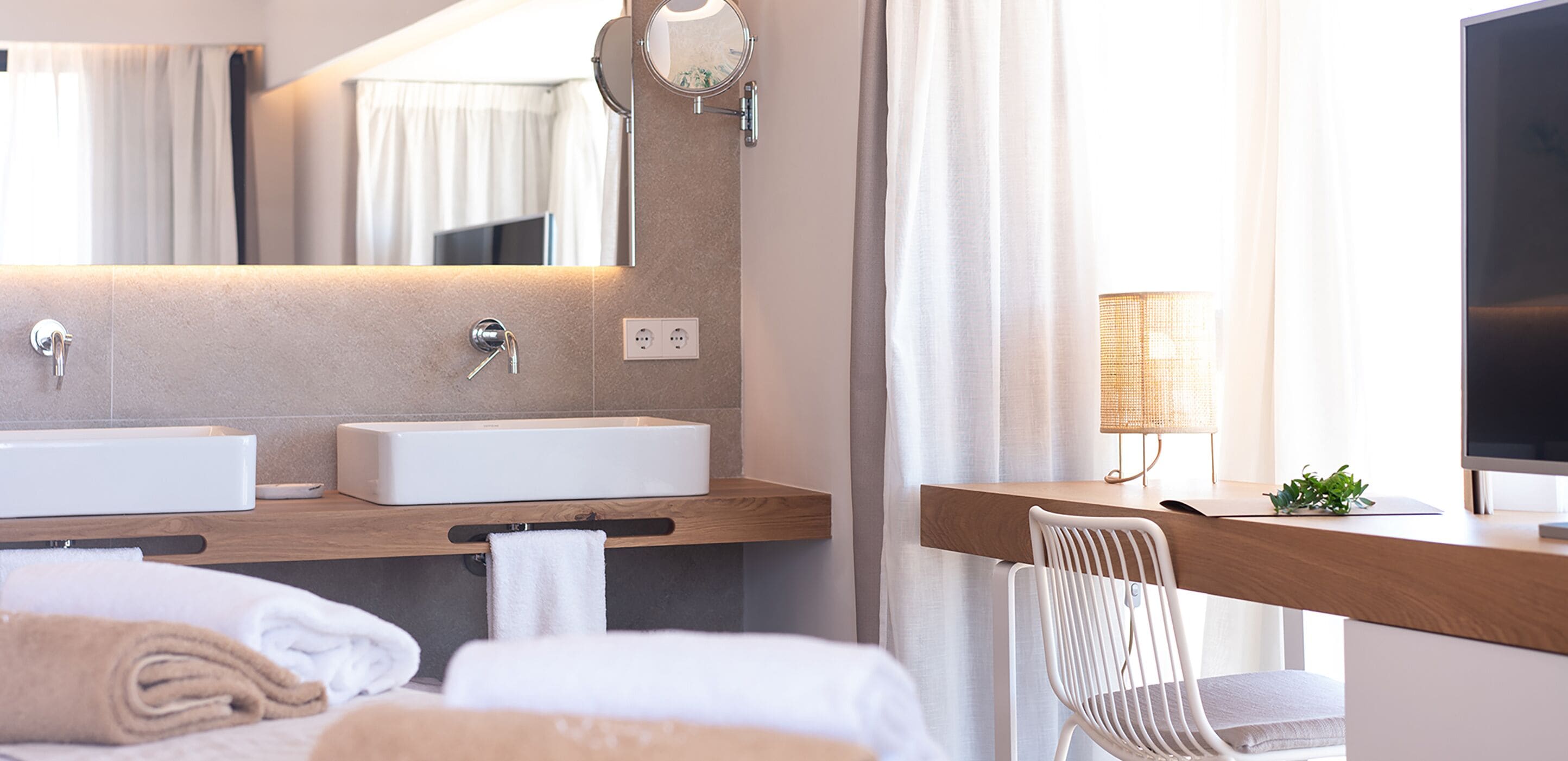 Une salle de bain moderne avec deux vasques, un miroir, un porte-serviettes et une table de chevet avec une lampe et une plante.
