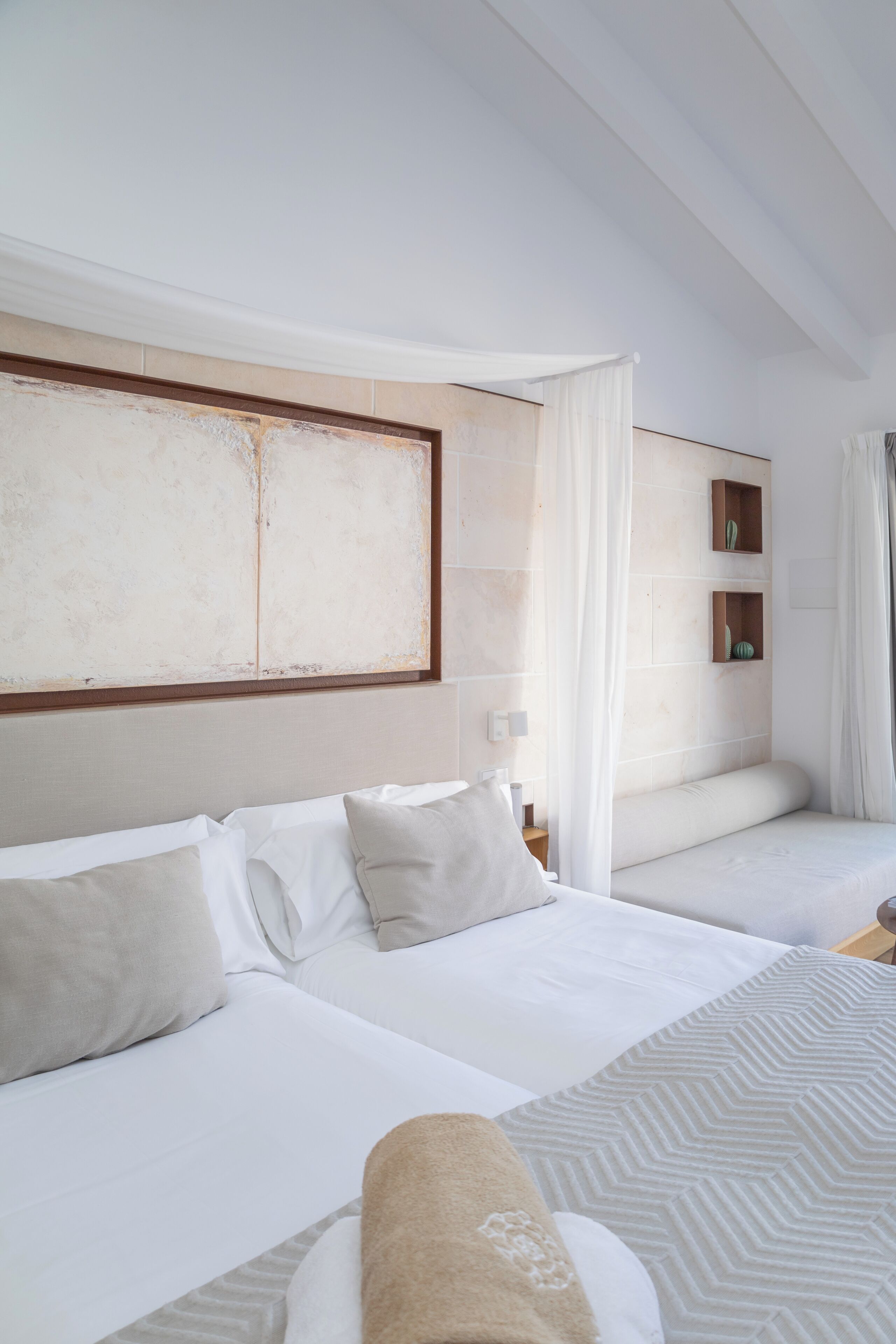 A hotel room with two beds, a large abstract painting on the wall, and a small cactus display.