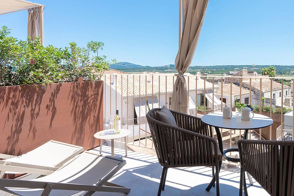A balcony with wicker chairs, a small round table, and a bottle of wine.