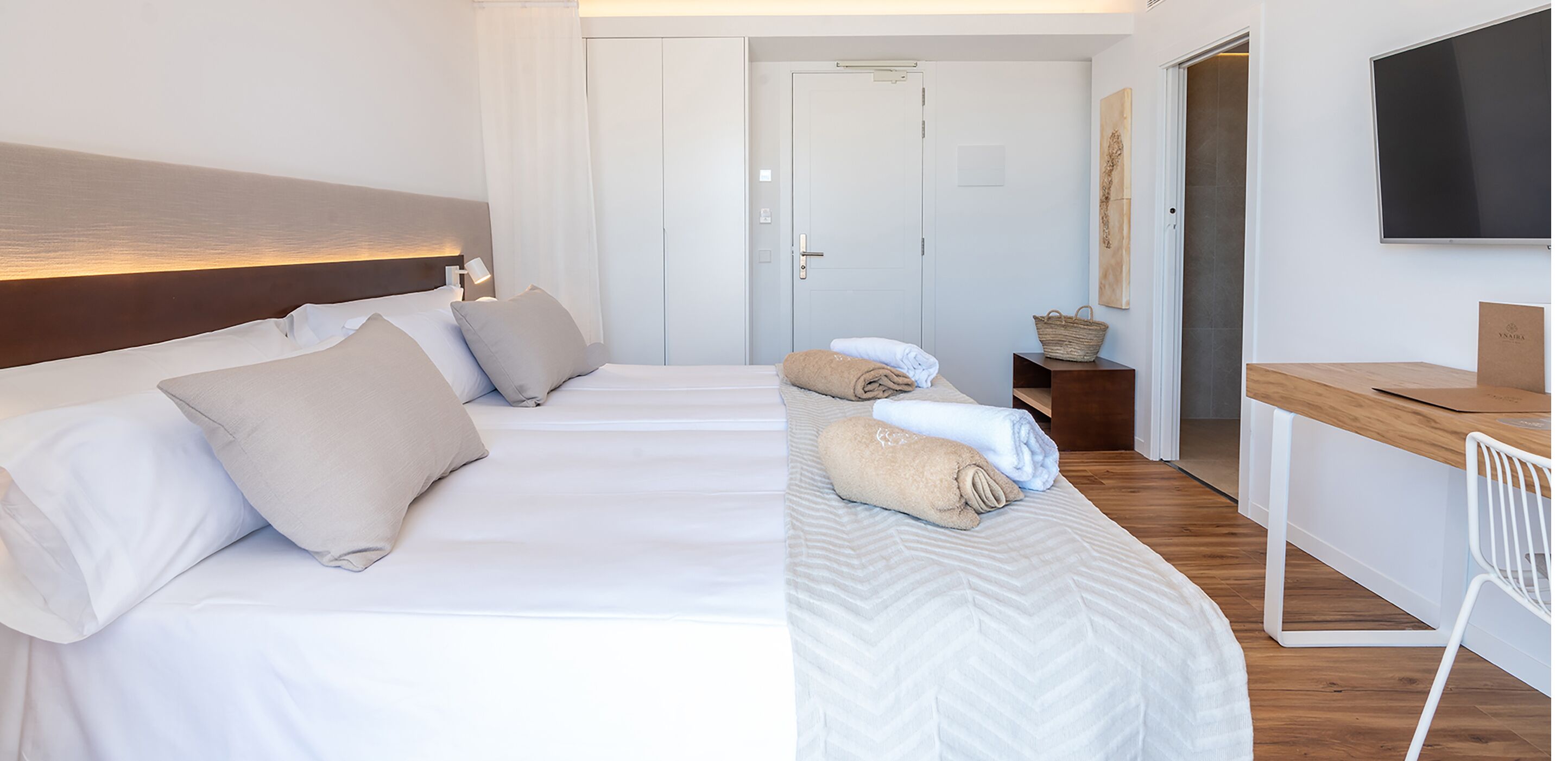 Una habitación de hotel con dos camas, un escritorio, una silla, un televisor y una puerta.