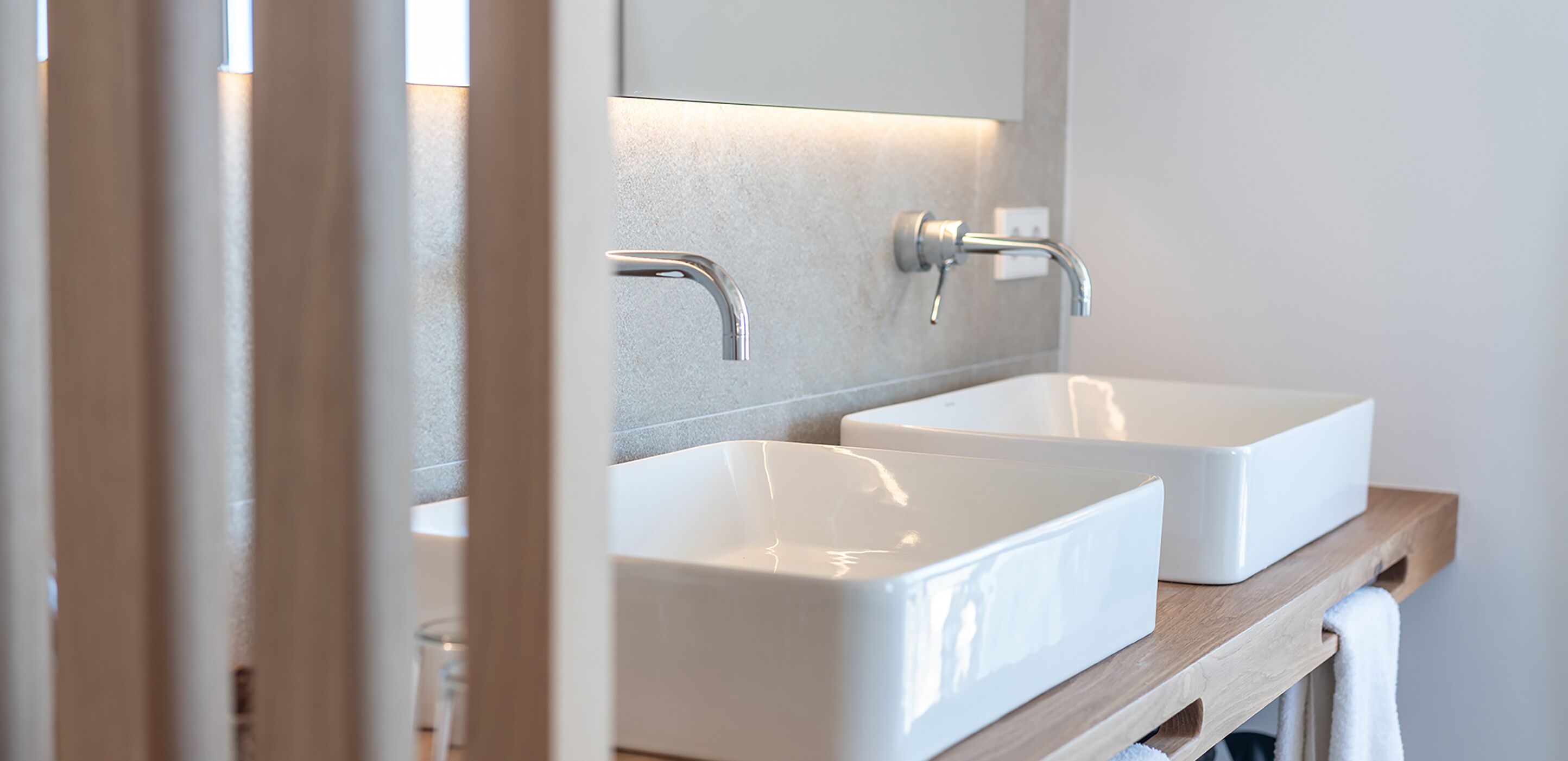 A bathroom with two white sinks, a mirror, and a wooden shelf.
