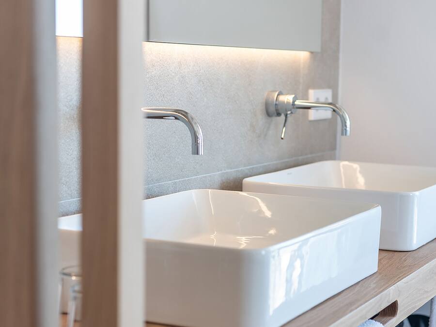 A bathroom with two white sinks, a mirror, and a wooden shelf.