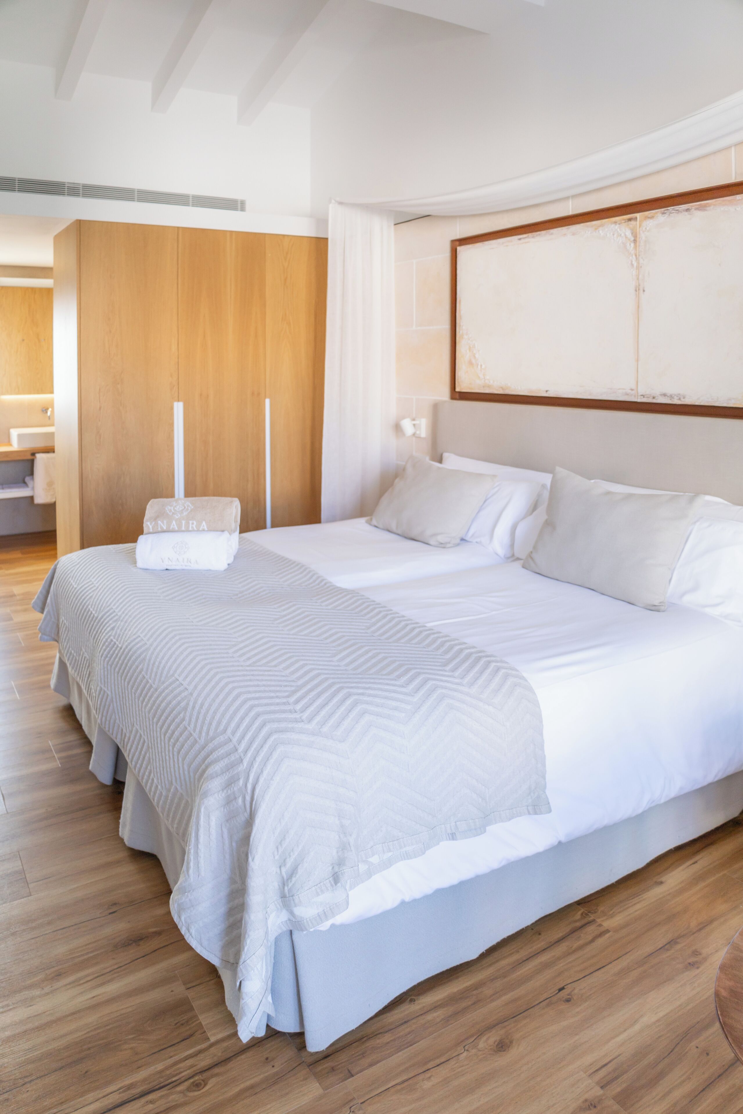 Een moderne hotelkamer met een groot bed, houten vloeren en een groot abstract schilderij aan de muur.
