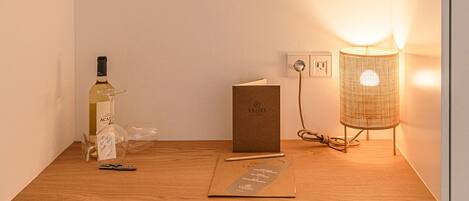 A wooden desk with a bottle, a book, a pen, and a lamp.