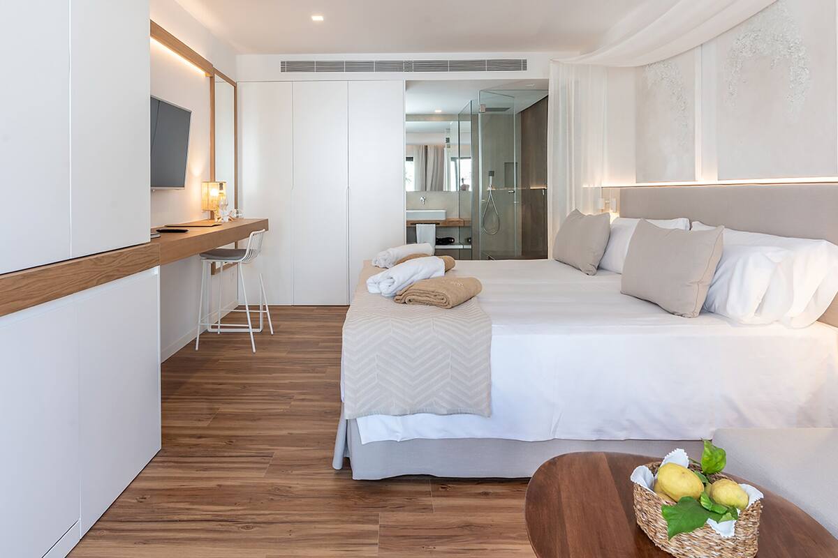 A hotel room with a bed, a desk, a chair, and a small table with fruit.