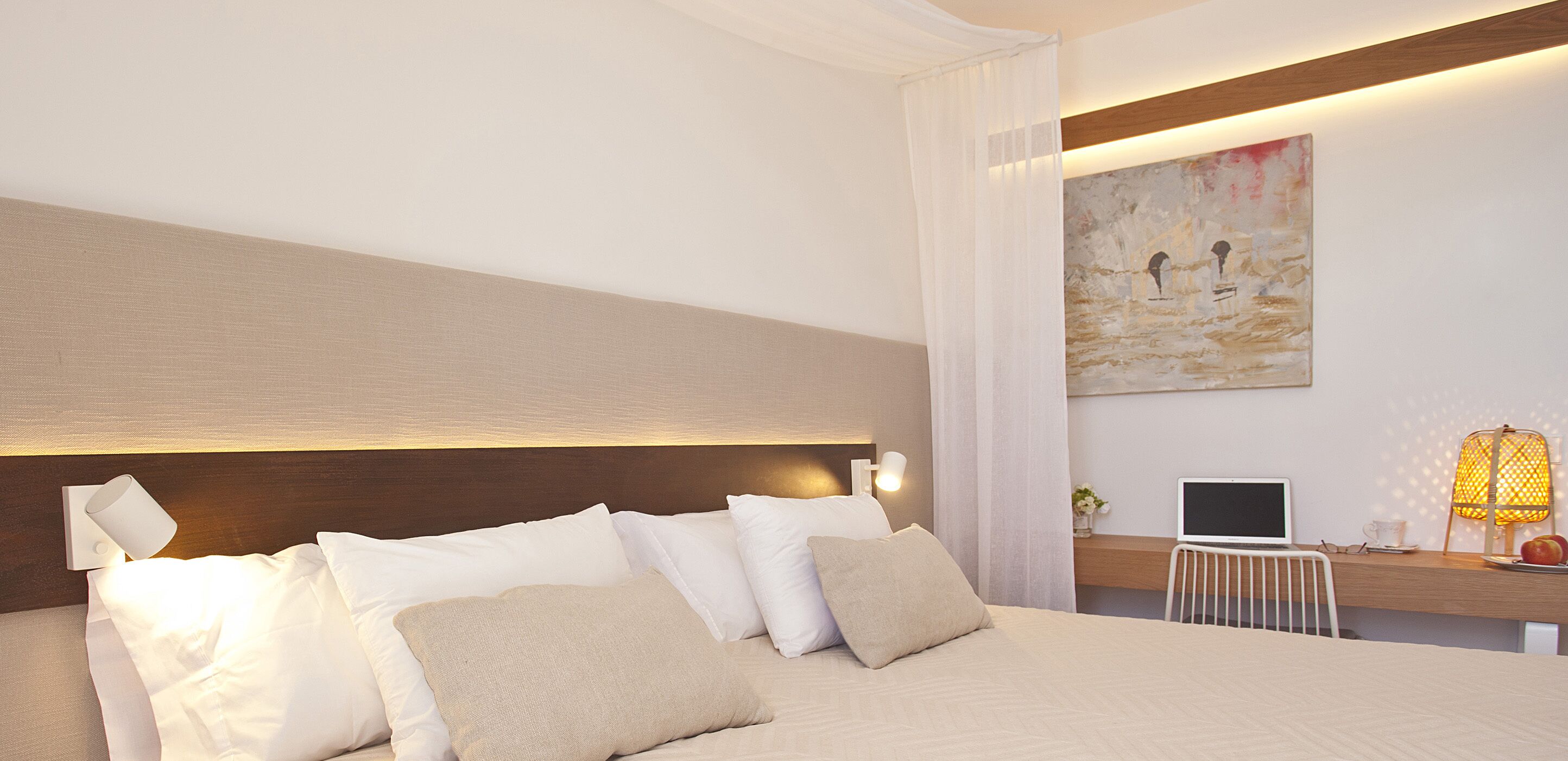 Una habitación de hotel moderna con una cama grande, un escritorio con una computadora portátil y un cuadro en la pared.