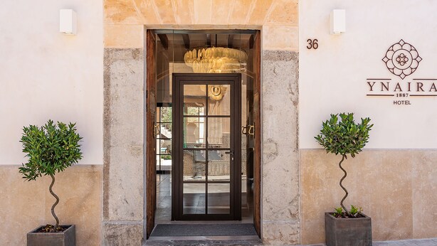 The entrance of Ynaira Hotel, featuring a glass door, a number 36 sign, and two potted plants. - Ynaira Hotel & Spa (Ariany)
