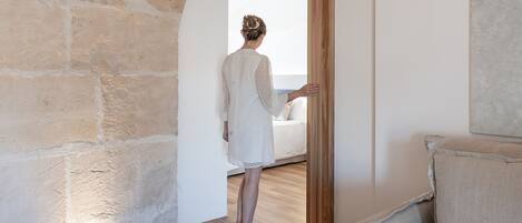 A room with a stone wall, a wooden door, and a bed with a white cover.