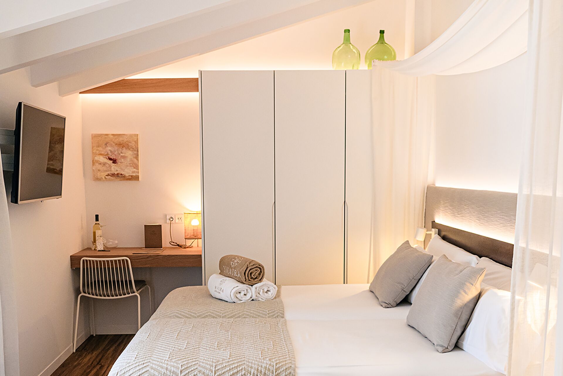 Een slaapkamer met een bed, een bureau, een stoel, een kledingkast en een schilderij aan de muur.