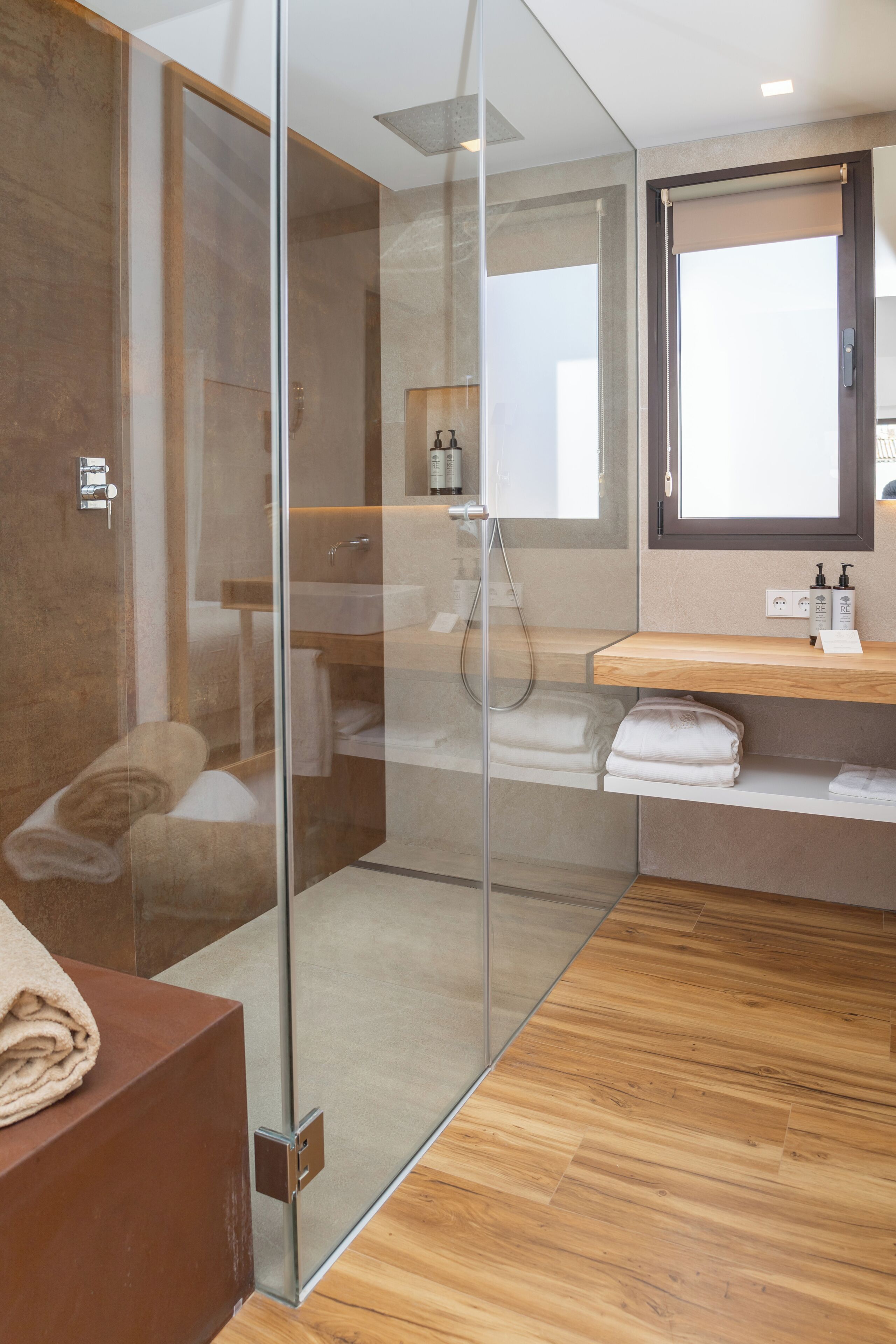 Un baño moderno con cabina de ducha de vidrio, suelo de madera, tocador de madera y un espejo grande.