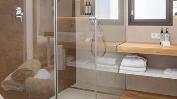 Un baño moderno con cabina de ducha de vidrio, suelo de madera, tocador de madera y un espejo grande.