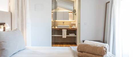 A hotel room with a bed, a bedside table, a mirror, a bathroom with a sink, and a towel rack.