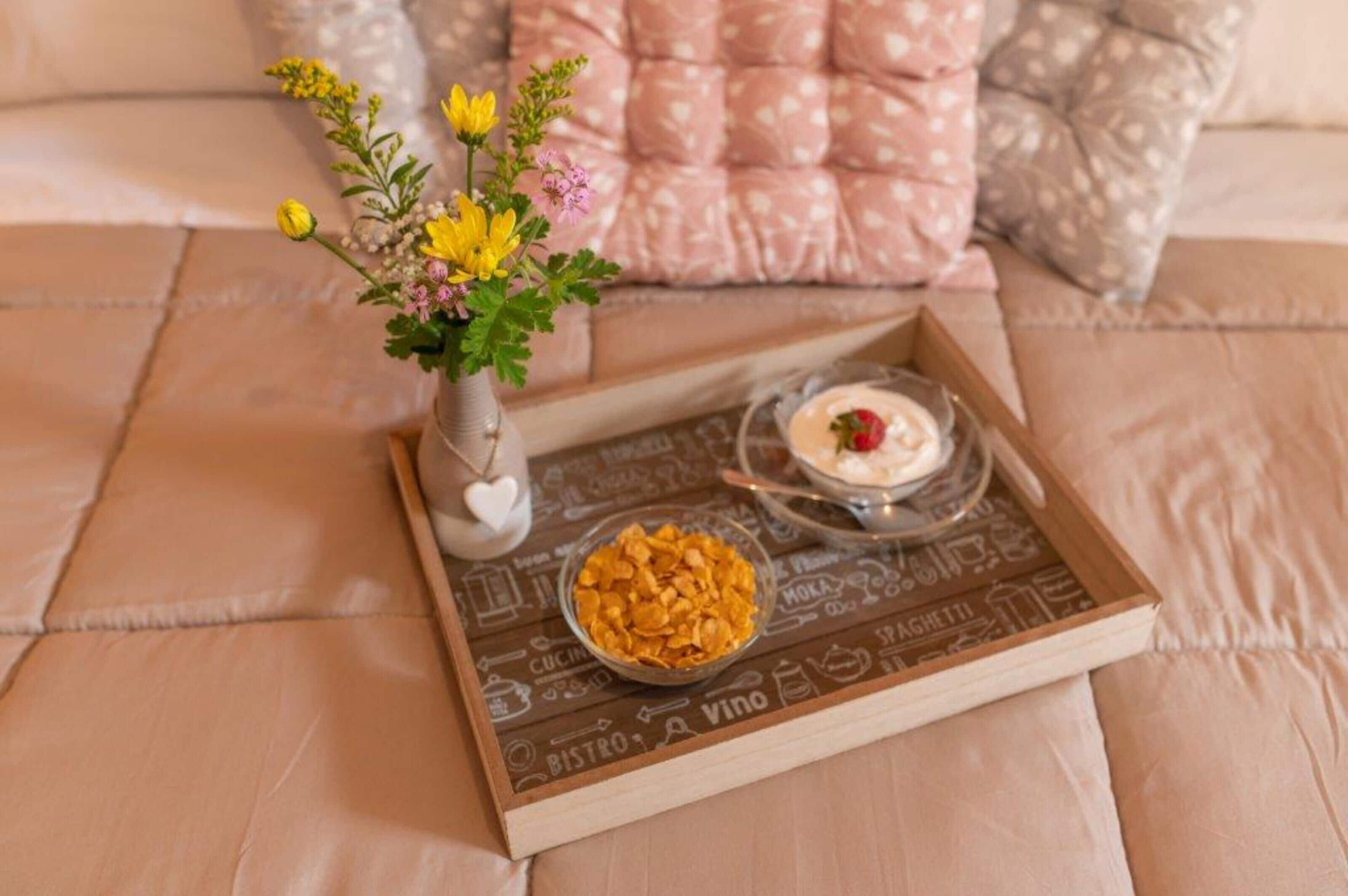 Ein Tablett mit Müsli und Dessert auf einem Bett mit einem Zierkissen.